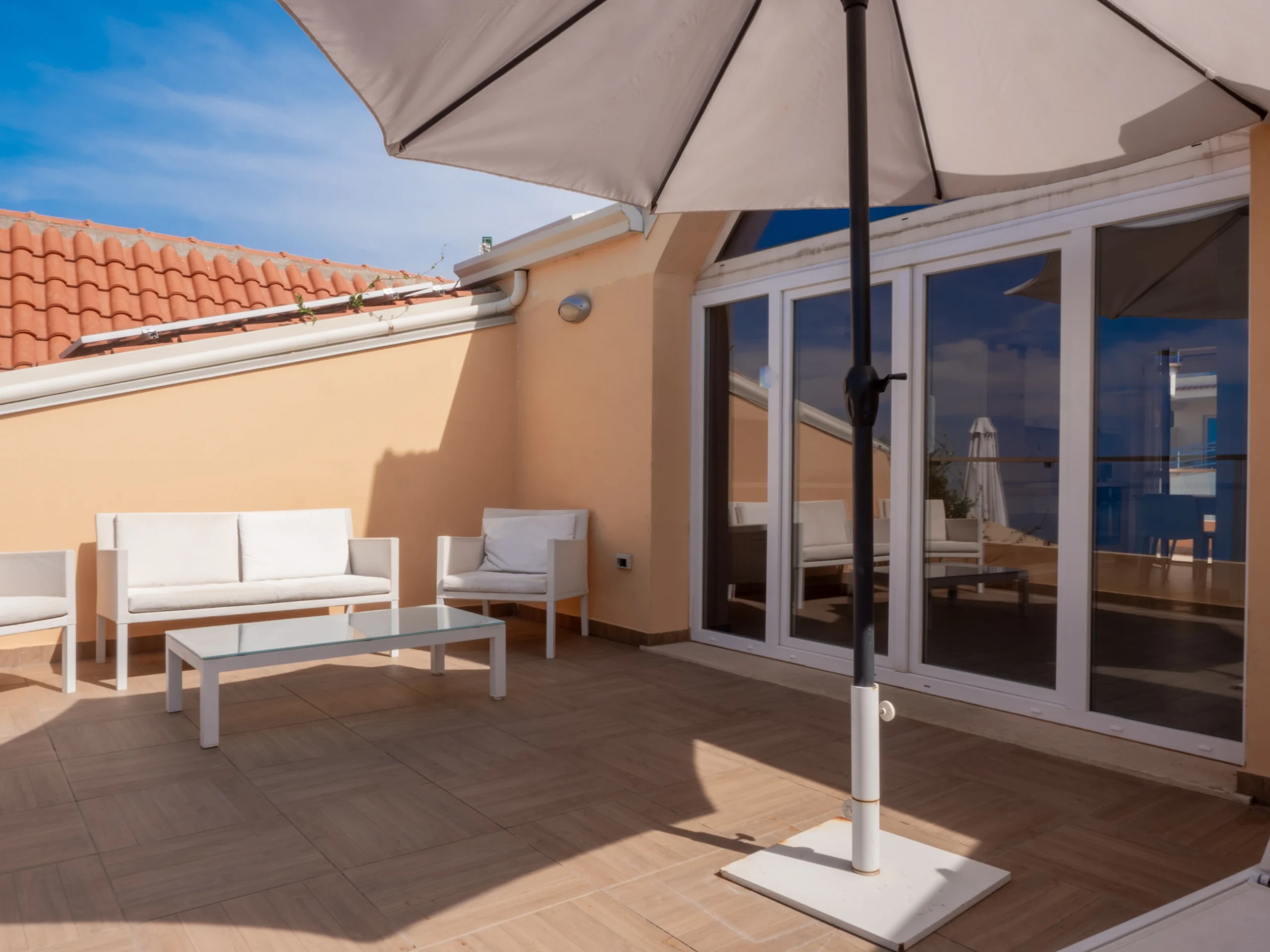 Ampio terrazzo privato arredato con divano, poltrone bianche e grande ombrellone all'Airone Residence Zambrone.