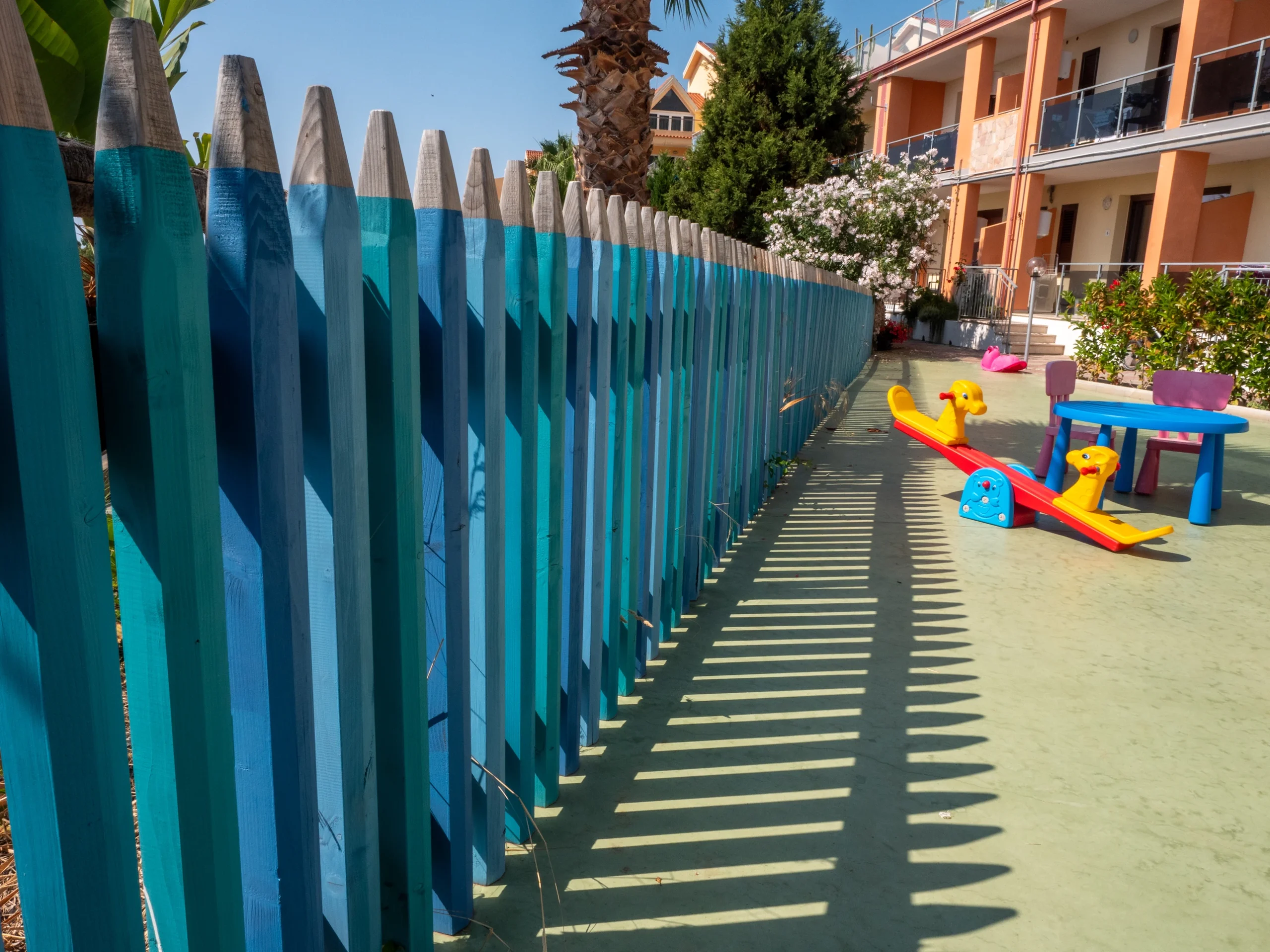 Area giochi per bambini con recinzione a forma di matite colorate, dondolo e tavolino all'aperto presso l'Airone Residence Zambrone.