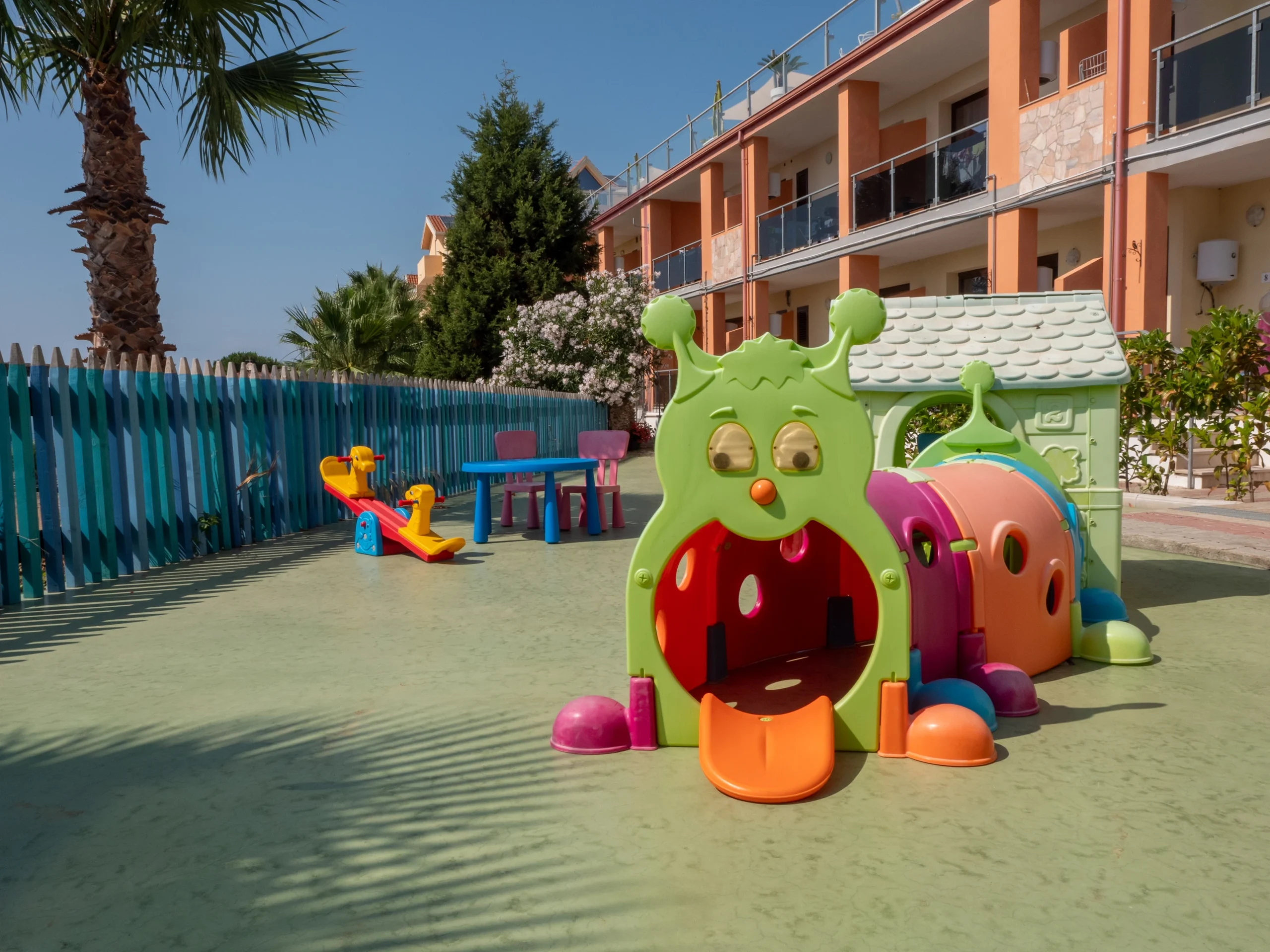 Area gioco all'aperto per bambini con tunnel a forma di bruco colorato, casetta giocattolo e dondolo presso l'Airone Residence Zambrone.