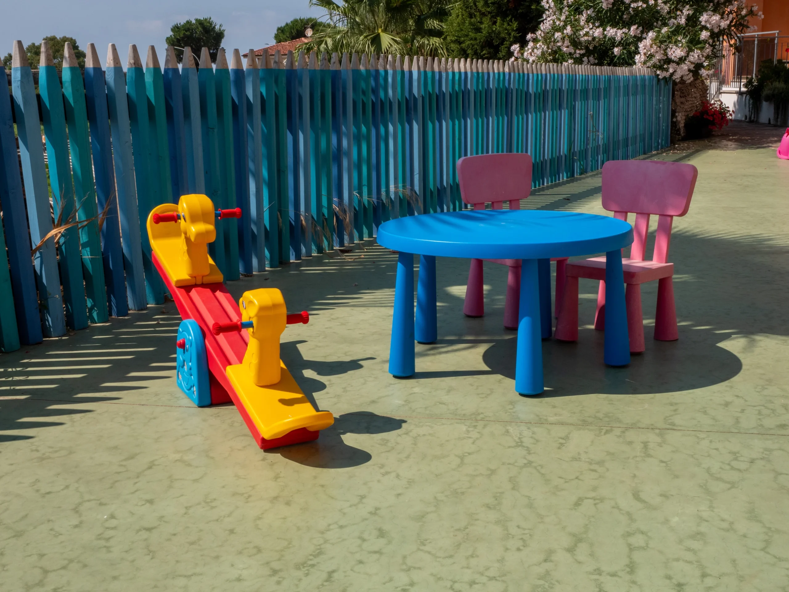 Area gioco bambini all'aperto dell'Airone Residence Zambrone con dondolo a bilico colorato, tavolino con seggioline e staccionata a forma di matite.