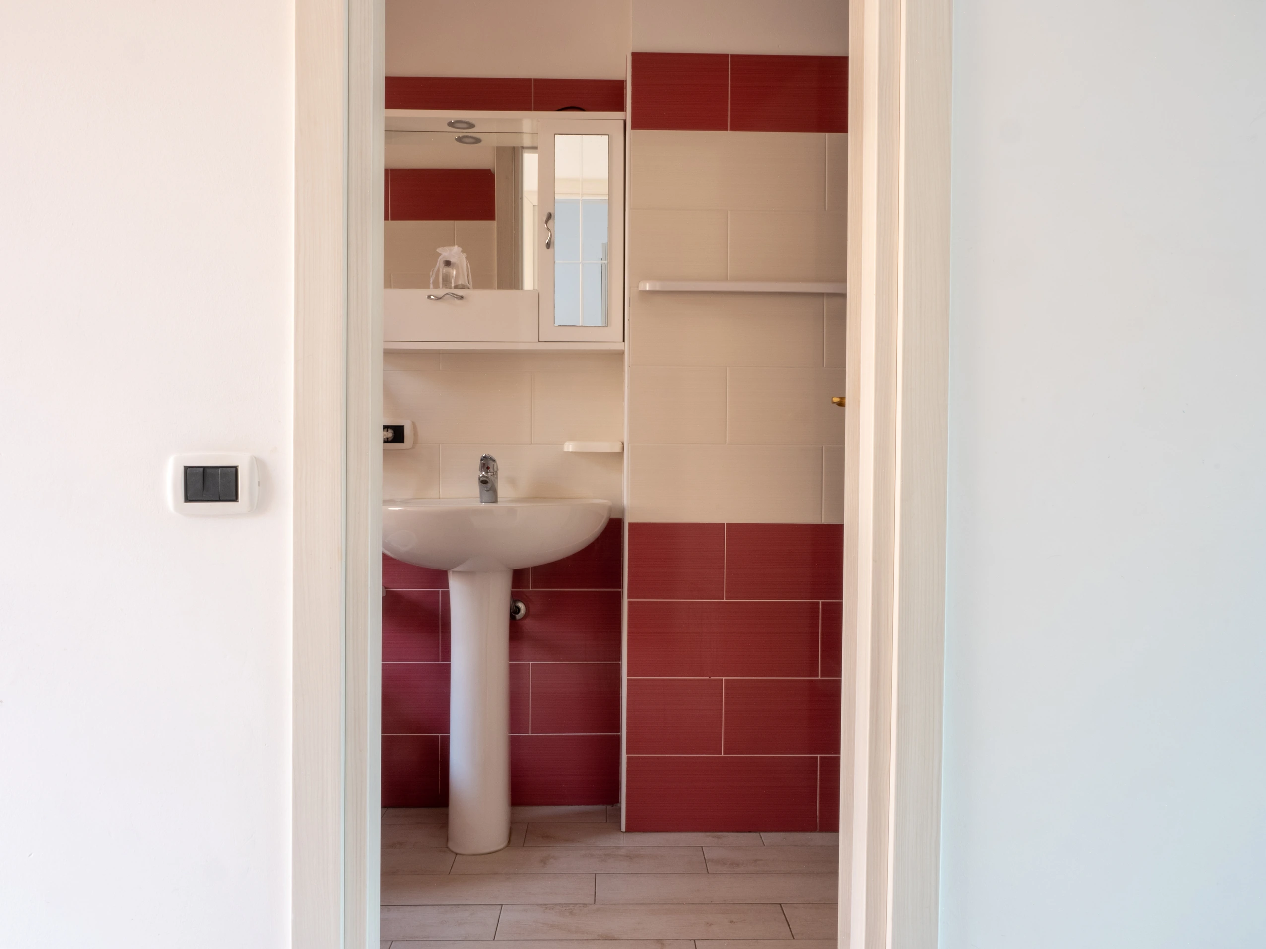Bagno moderno con piastrelle rosse e bianche, lavandino a colonna e specchio in un appartamento dell'Airone Residence Zambrone.