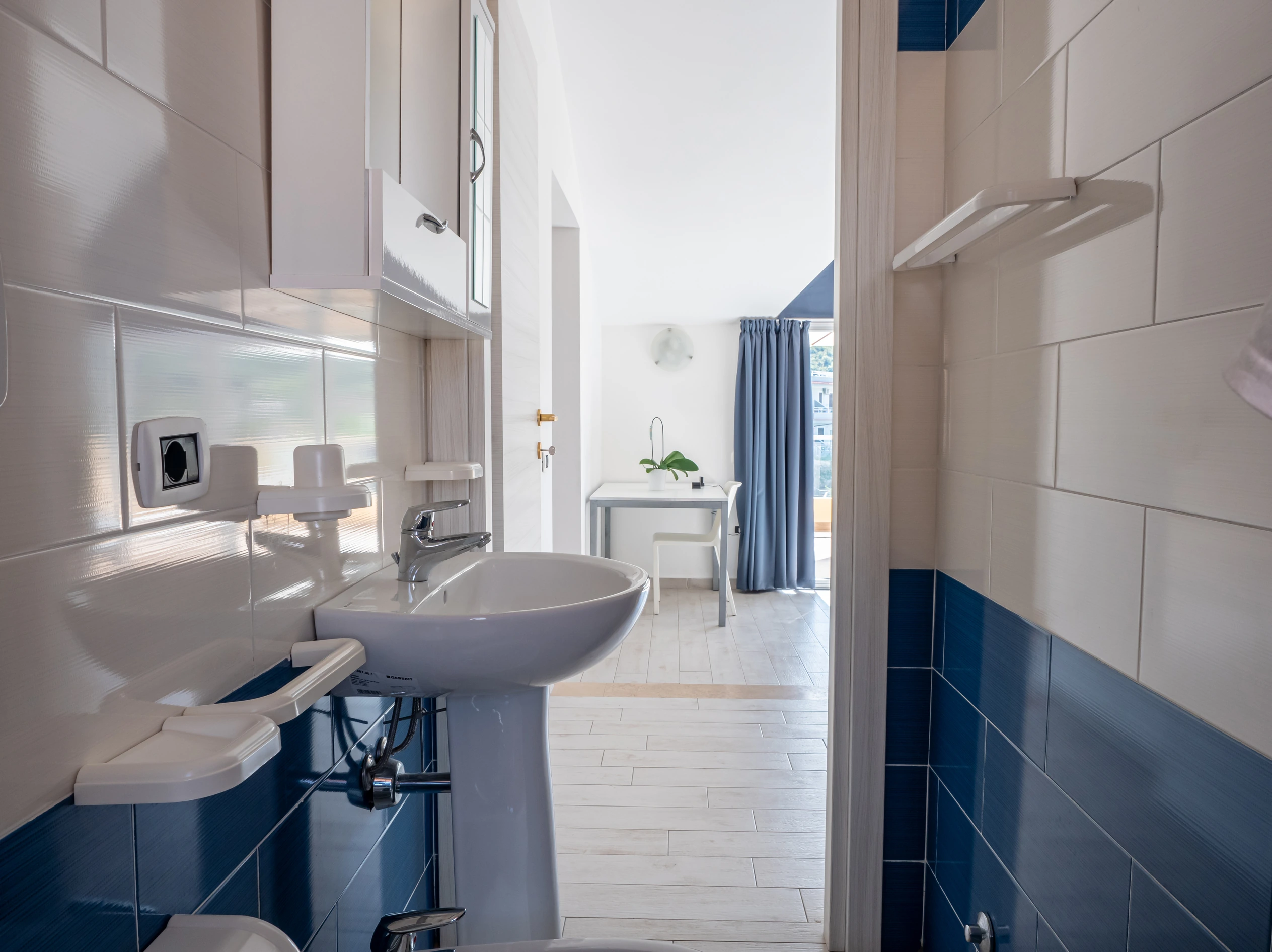 Interno del bagno moderno con piastrelle bianche e blu dell'Airone Residence Zambrone, con vista sulla luminosa zona giorno.
