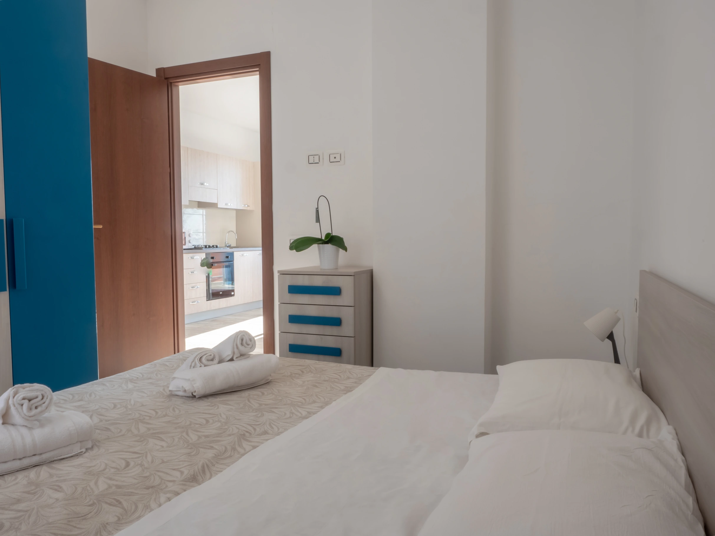 Camera da letto matrimoniale con asciugamani sul letto, cassettiera moderna e porta aperta sulla cucina all'Airone Residence Zambrone.