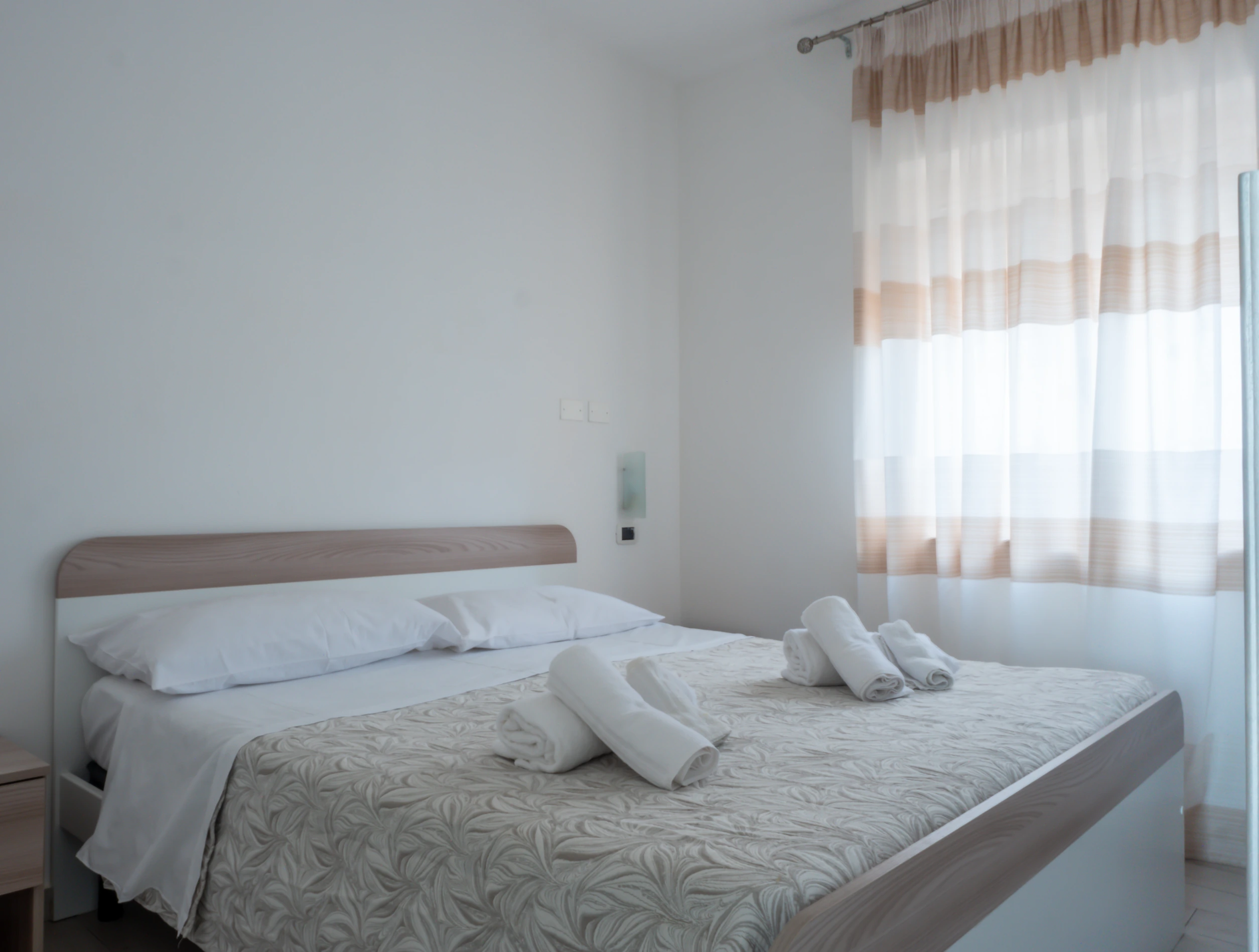 camera da letto matrimoniale con asciugamani bianchi sul letto e tenda a righe in un appartamento dell'Airone Residence Zambrone