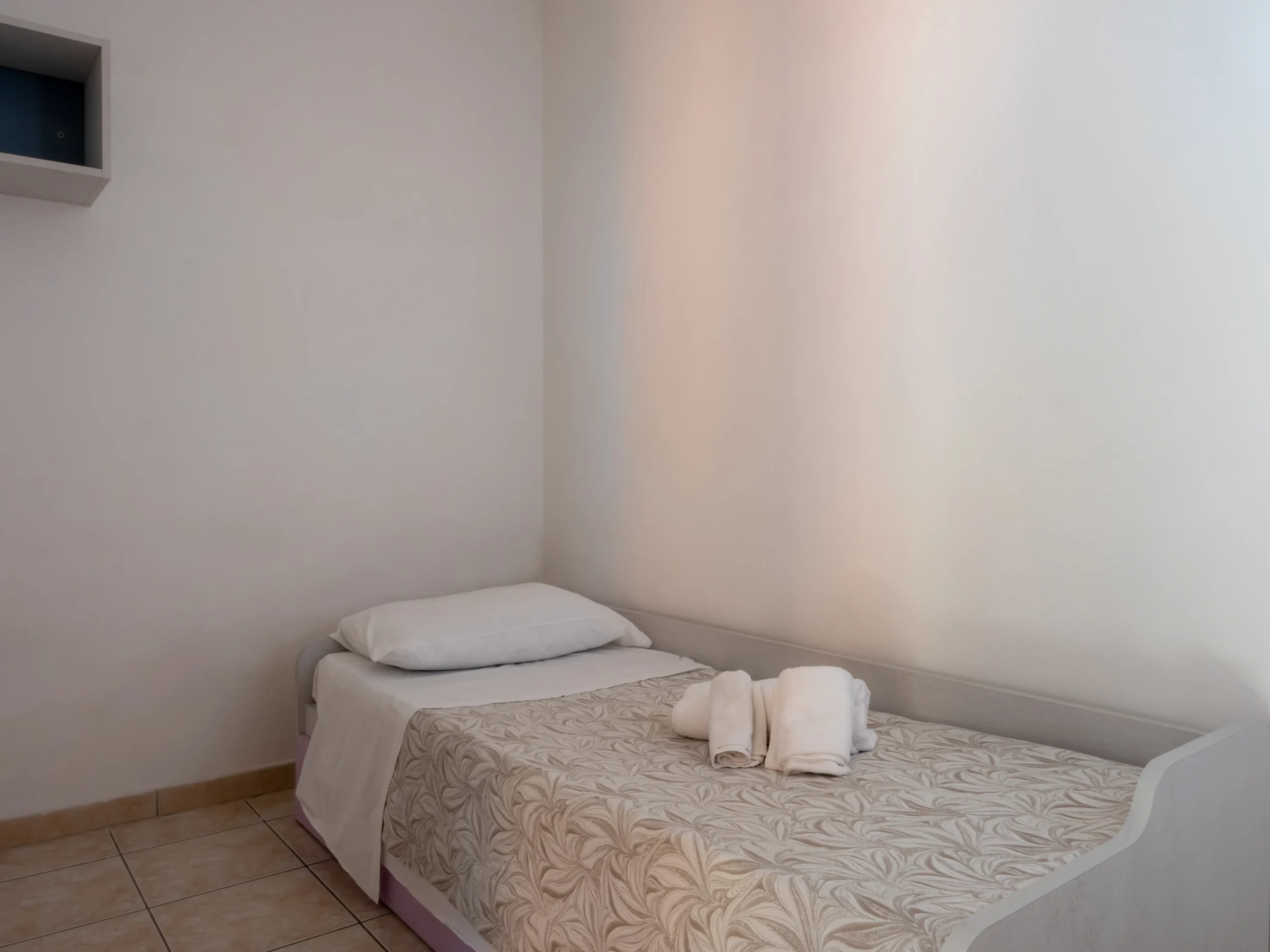 Cameretta con letto singolo, asciugamani bianchi in spugna e copriletto decorato nel trilocale dell'Airone Residence Zambrone.