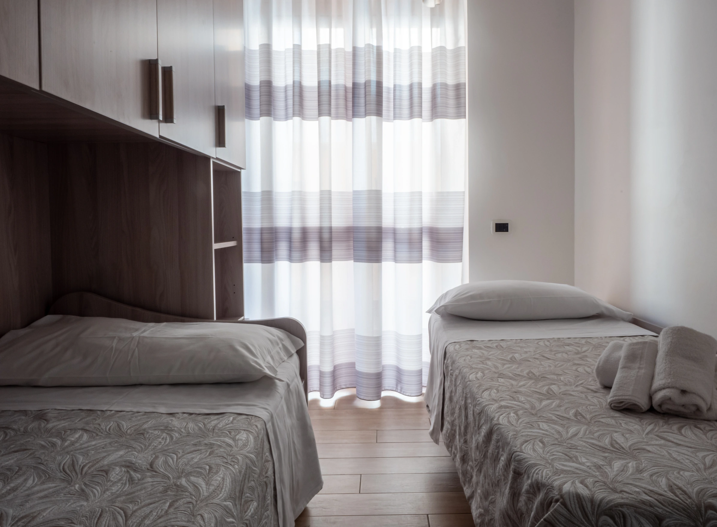 Cameretta doppia con due letti singoli, armadio a ponte in legno e finestra con tenda a righe all'Airone Residence Zambrone.