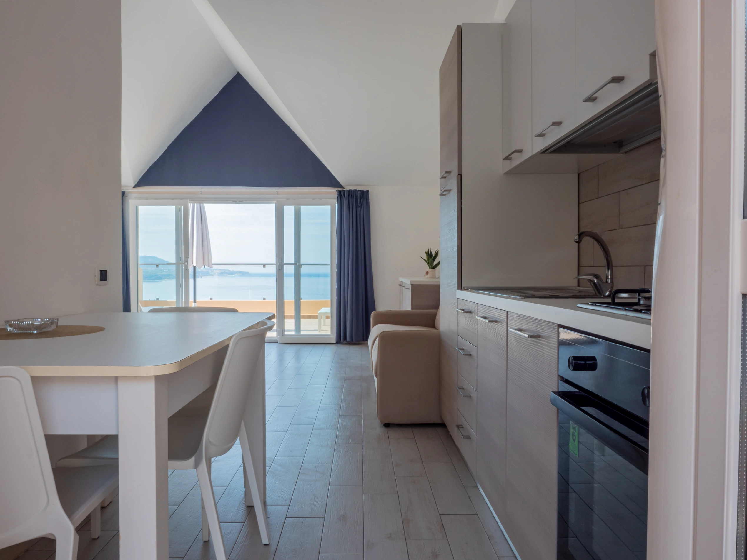 Interno di un appartamento bilocale all'Airone Residence Zambrone con angolo cottura, tavolo da pranzo e grande vetrata aperta sul terrazzo vista mare.