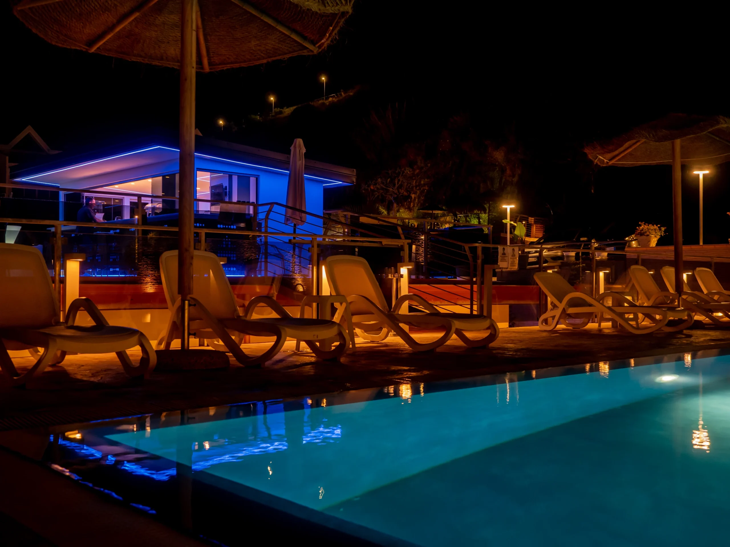 Piscina illuminata di notte con lettini a bordo vasca e lounge bar retroilluminato con LED blu all'Airone Residence Zambrone.