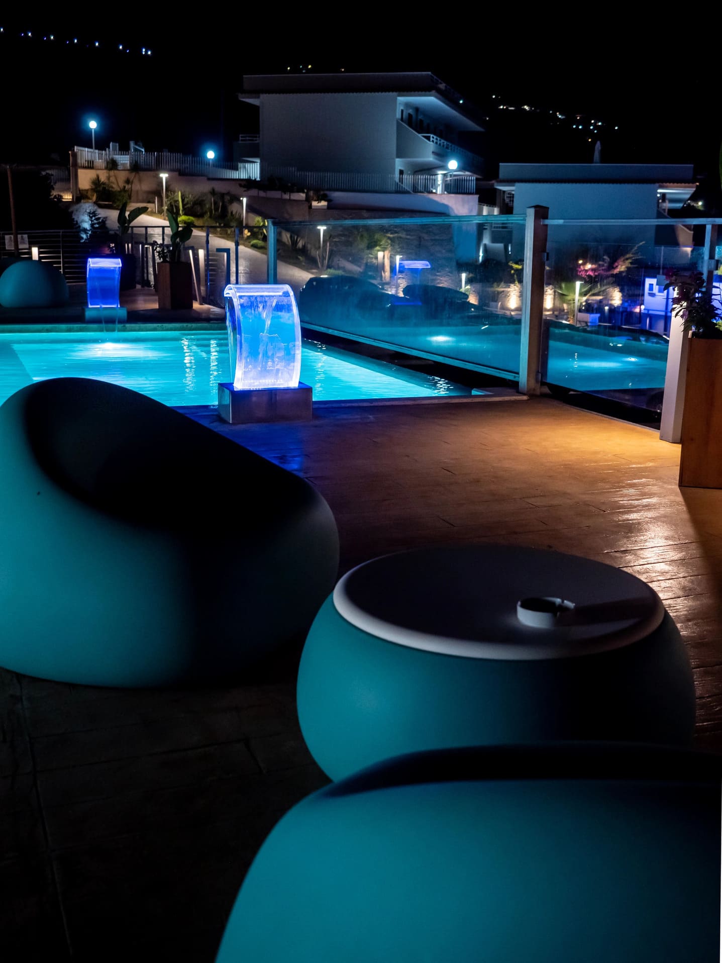 Piscina illuminata di notte con fontane a cascata e moderne sedute lounge sulla terrazza dell'Airone Residence Zambrone in Calabria.