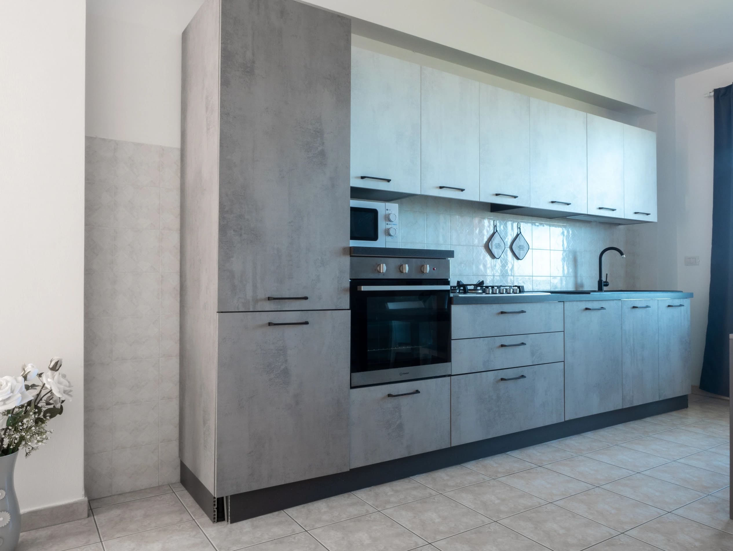 Cucina componibile moderna con finitura effetto cemento grigio, pensili chiari ed elettrodomestici integrati all'Airone Residence Zambrone.