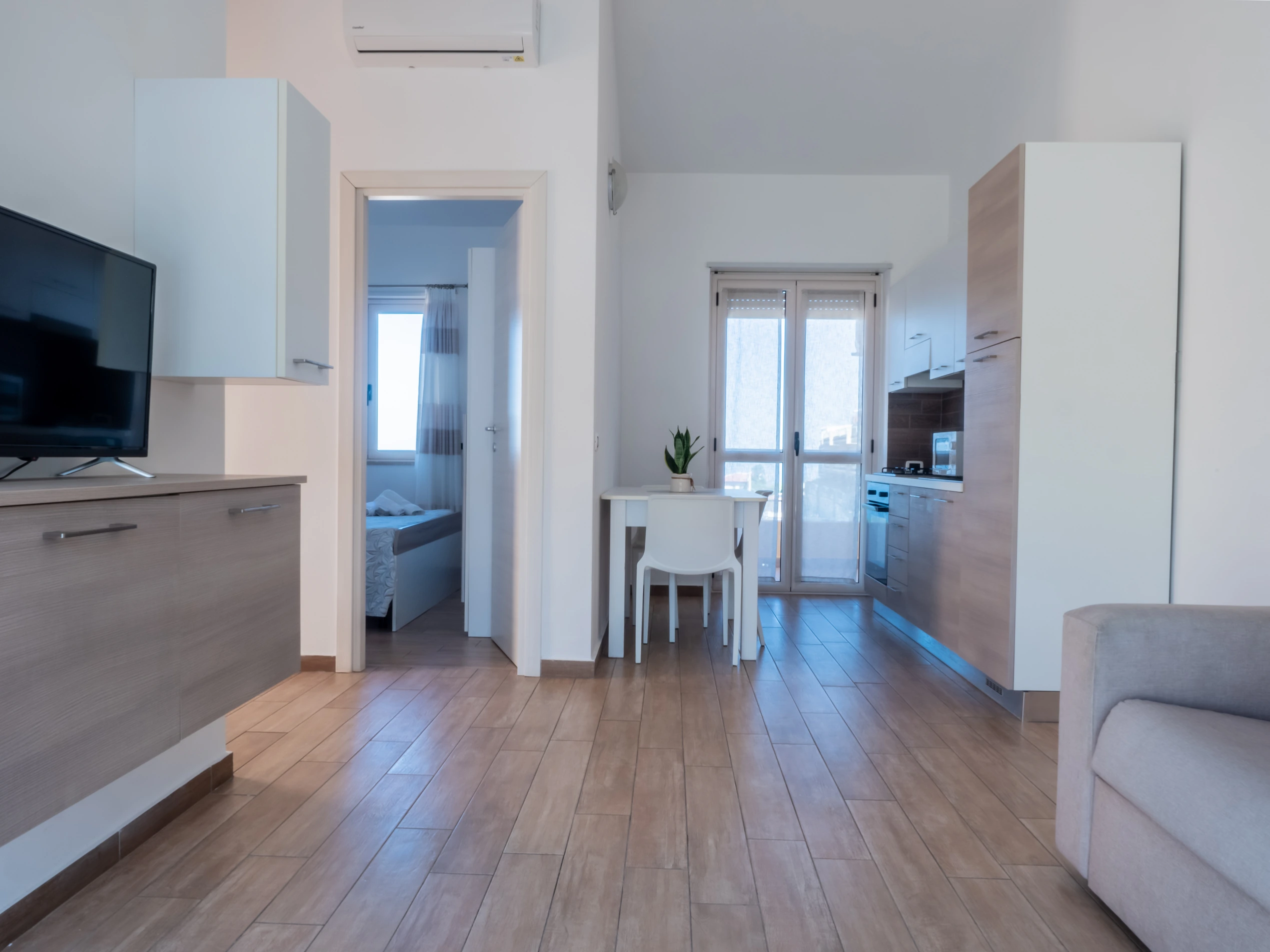 Ampio soggiorno open space moderno all'Airone Residence Zambrone con vista su cucina, tavolo da pranzo, climatizzatore e porta aperta sulla camera da letto.