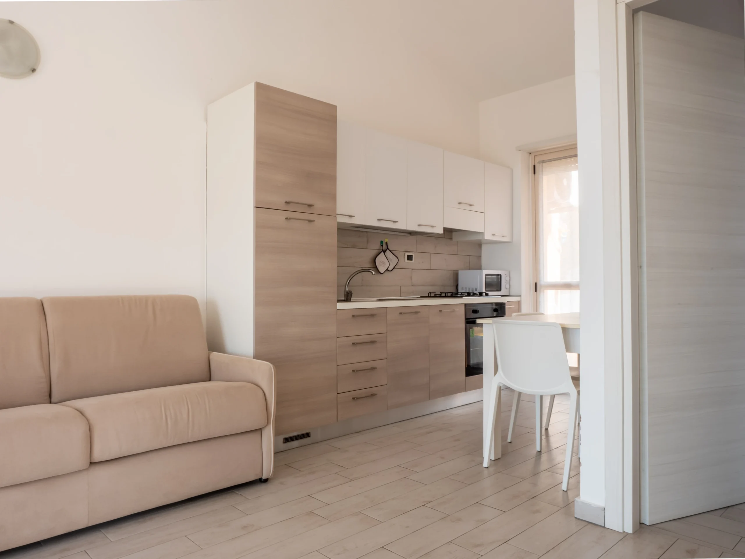 Soggiorno open space di un appartamento bilocale all'Airone Residence Zambrone con divano beige, mobile TV e cucina lineare moderna.