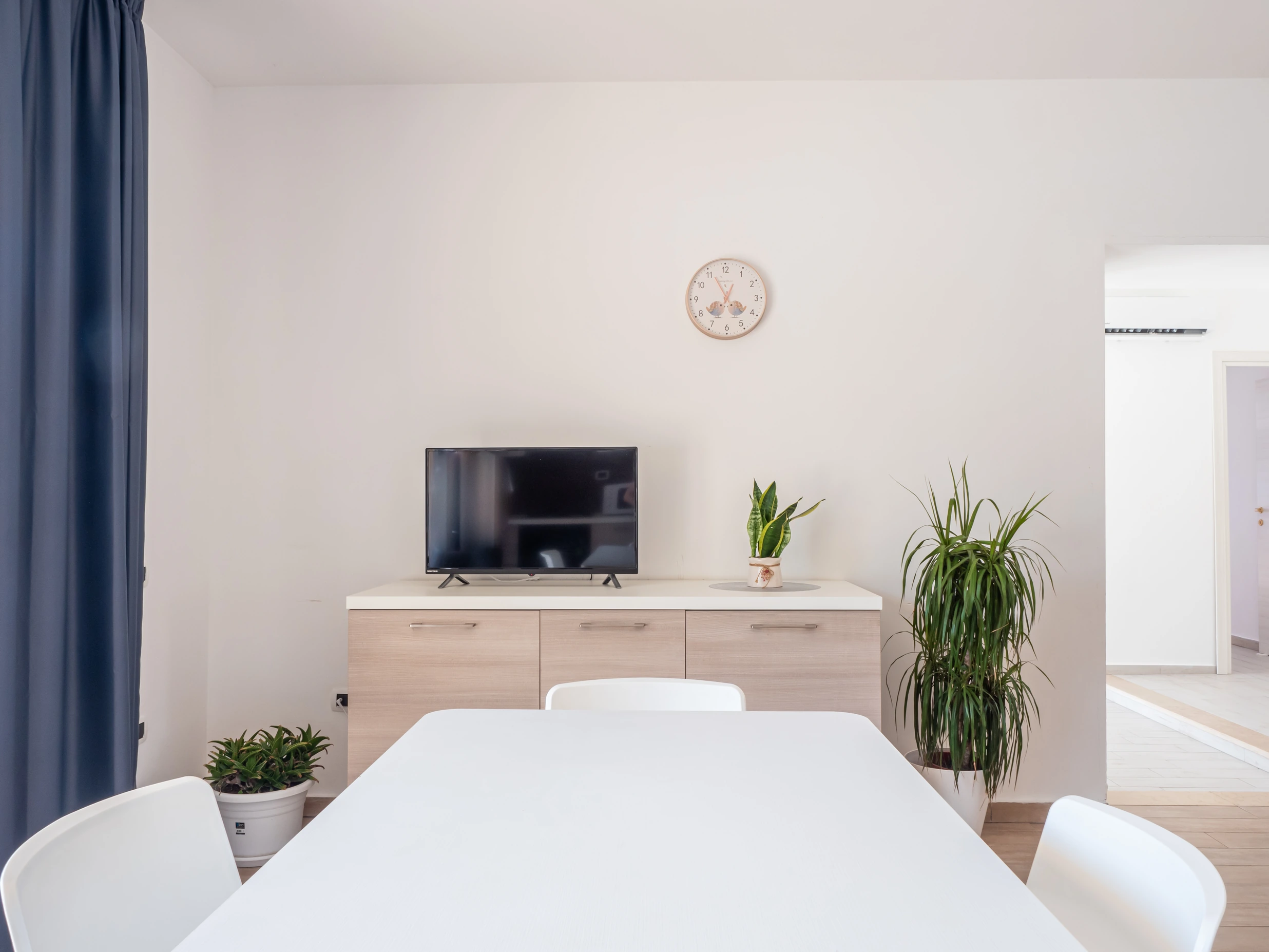 Tavolo da pranzo bianco e mobile TV in legno chiaro nel soggiorno moderno dell'Airone Residence Zambrone.