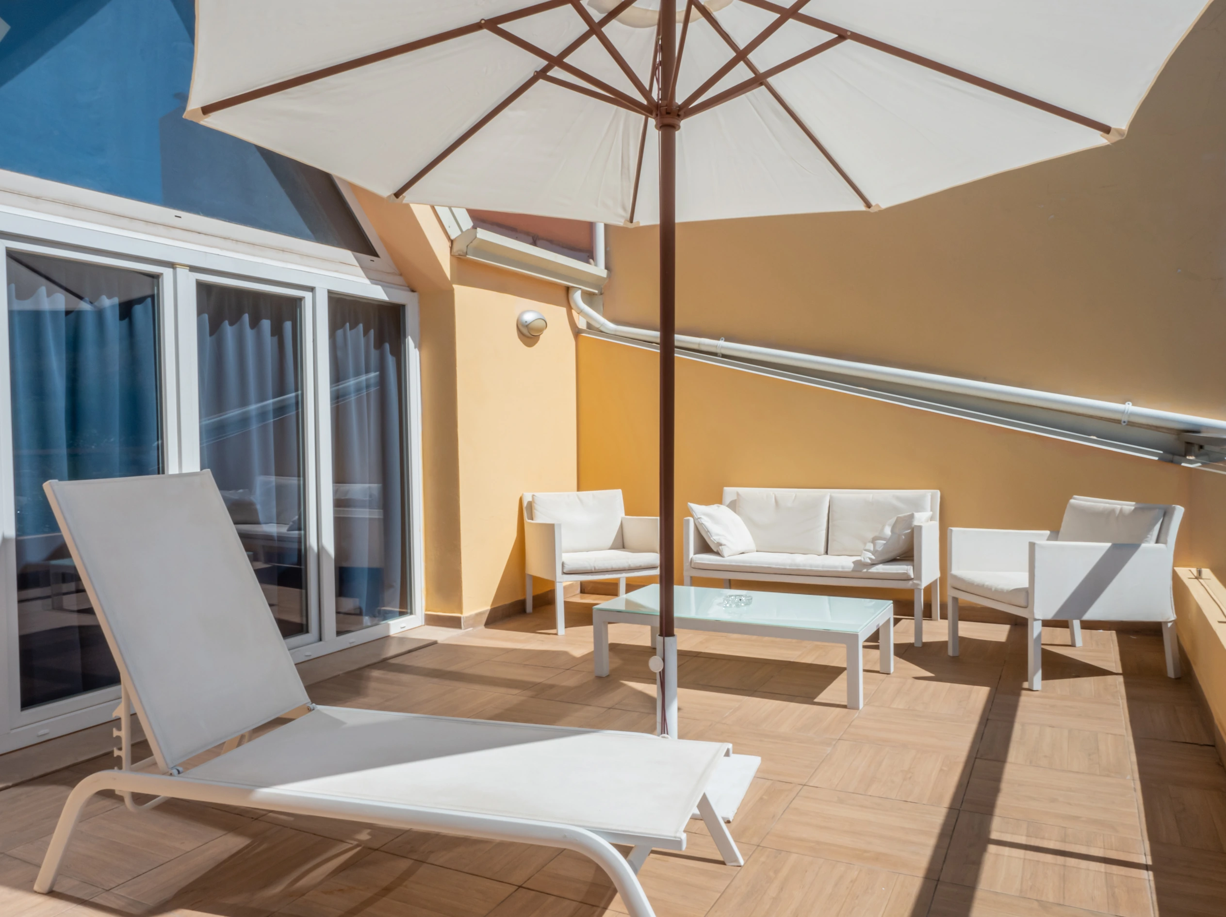 Terrazzo solarium privato dell'Airone Residence Zambrone arredato con lettino prendisole bianco, grande ombrellone e salottino da esterno.