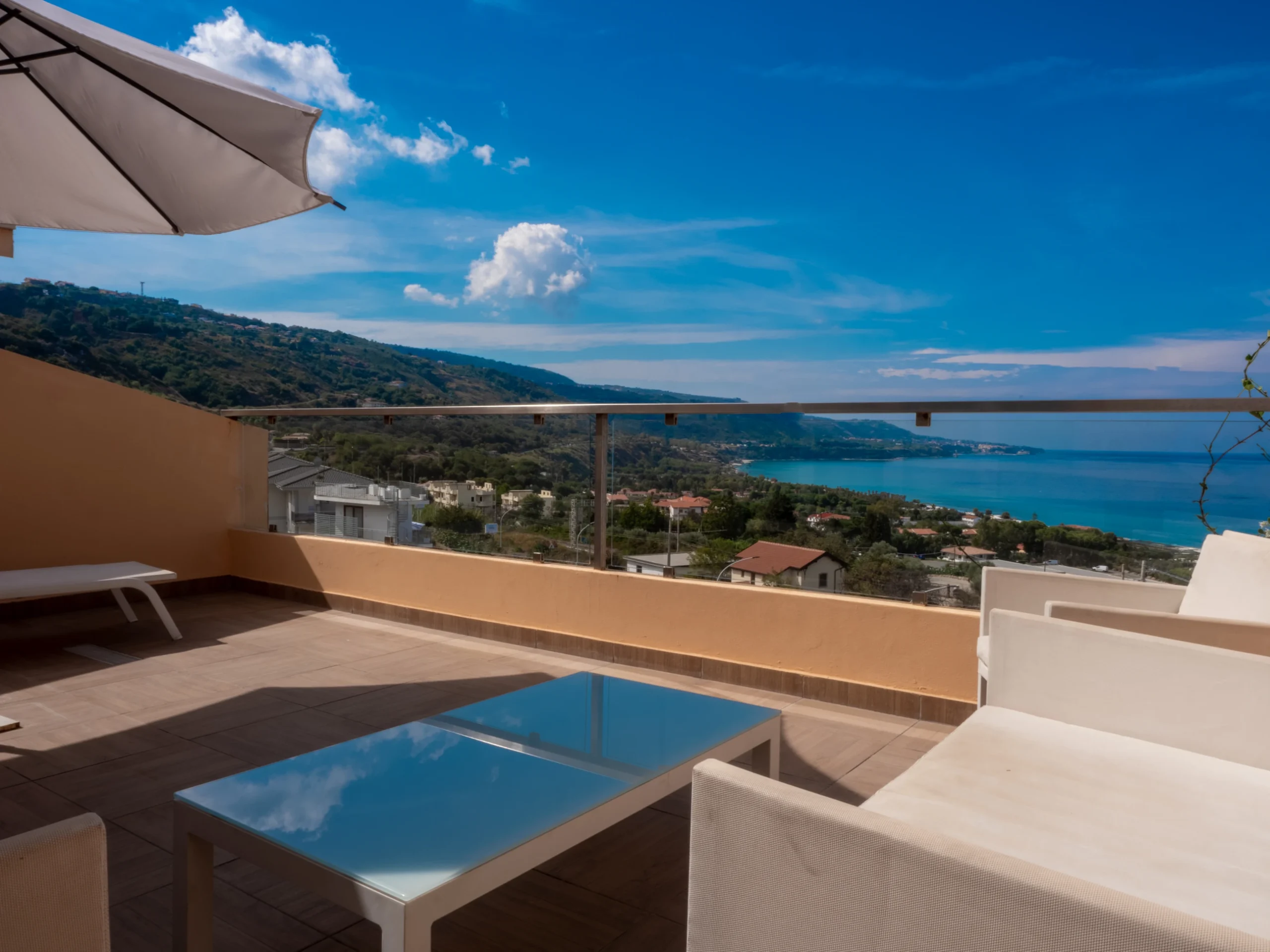 Terrazzo privato e panoramico del bilocale all'Airone Residence Zambrone, attrezzato con tavolo e sedie da esterno bianche e splendida vista sul mare.