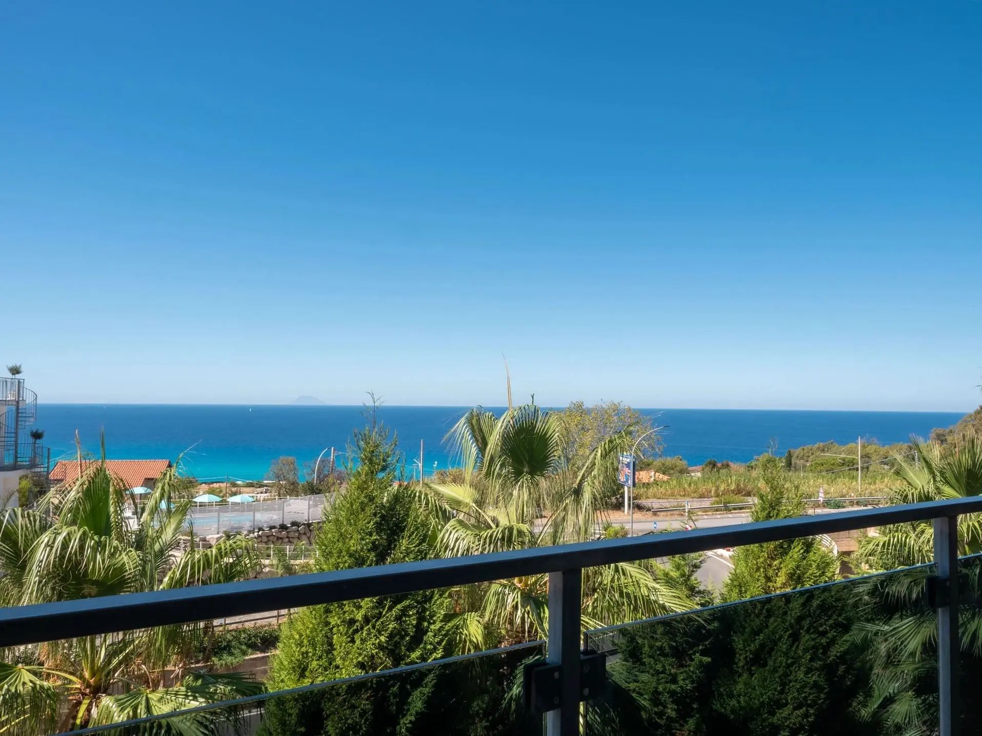 Splendida vista panoramica sul mare azzurro e cristallino dal terrazzo con ringhiera moderna dell'Airone Residence Zambrone, circondato da palme.
