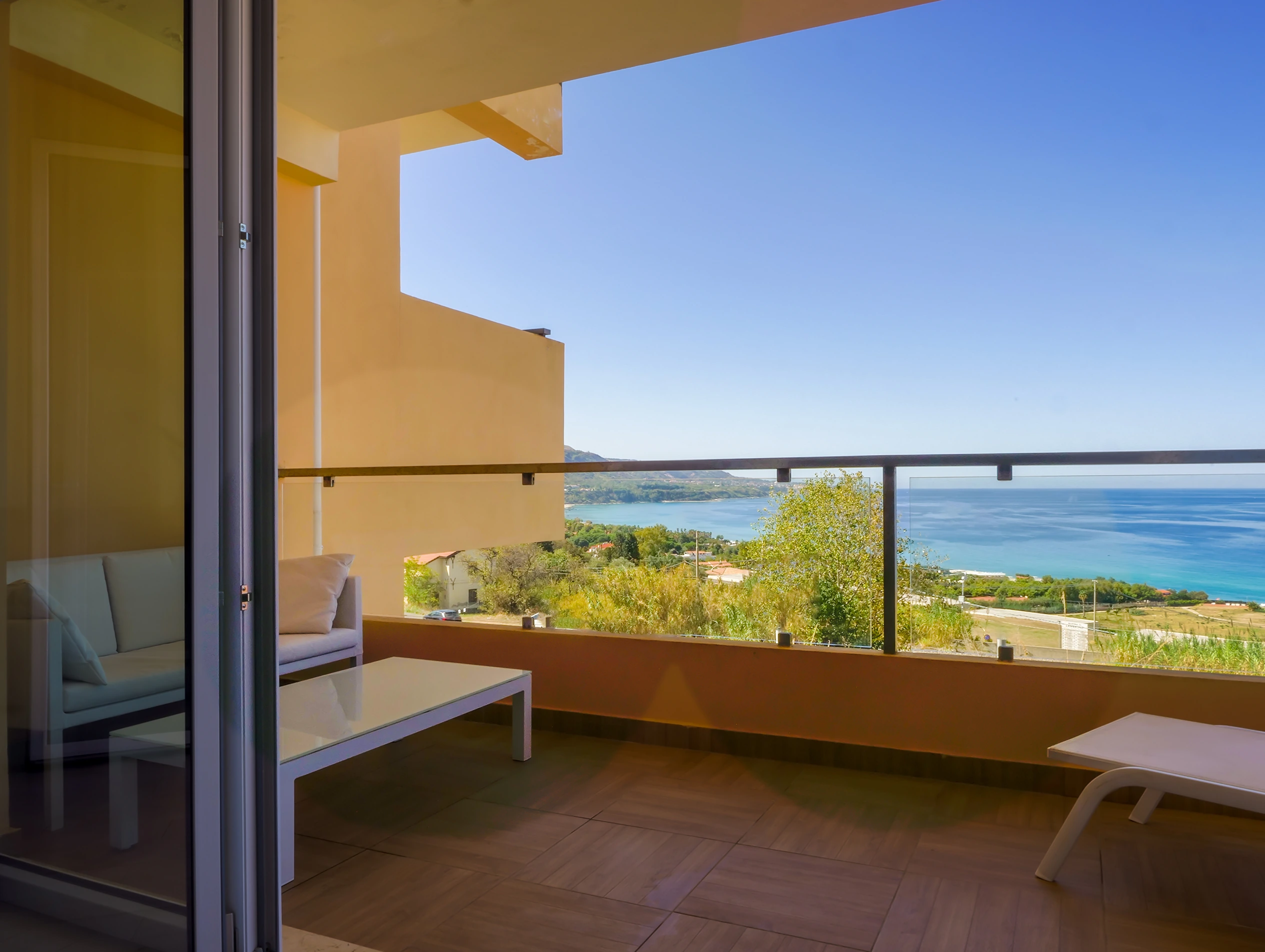 Elegante divano esterno bianco su un terrazzo privato con fiori di bouganville e vista sul mare azzurro di Zambrone.