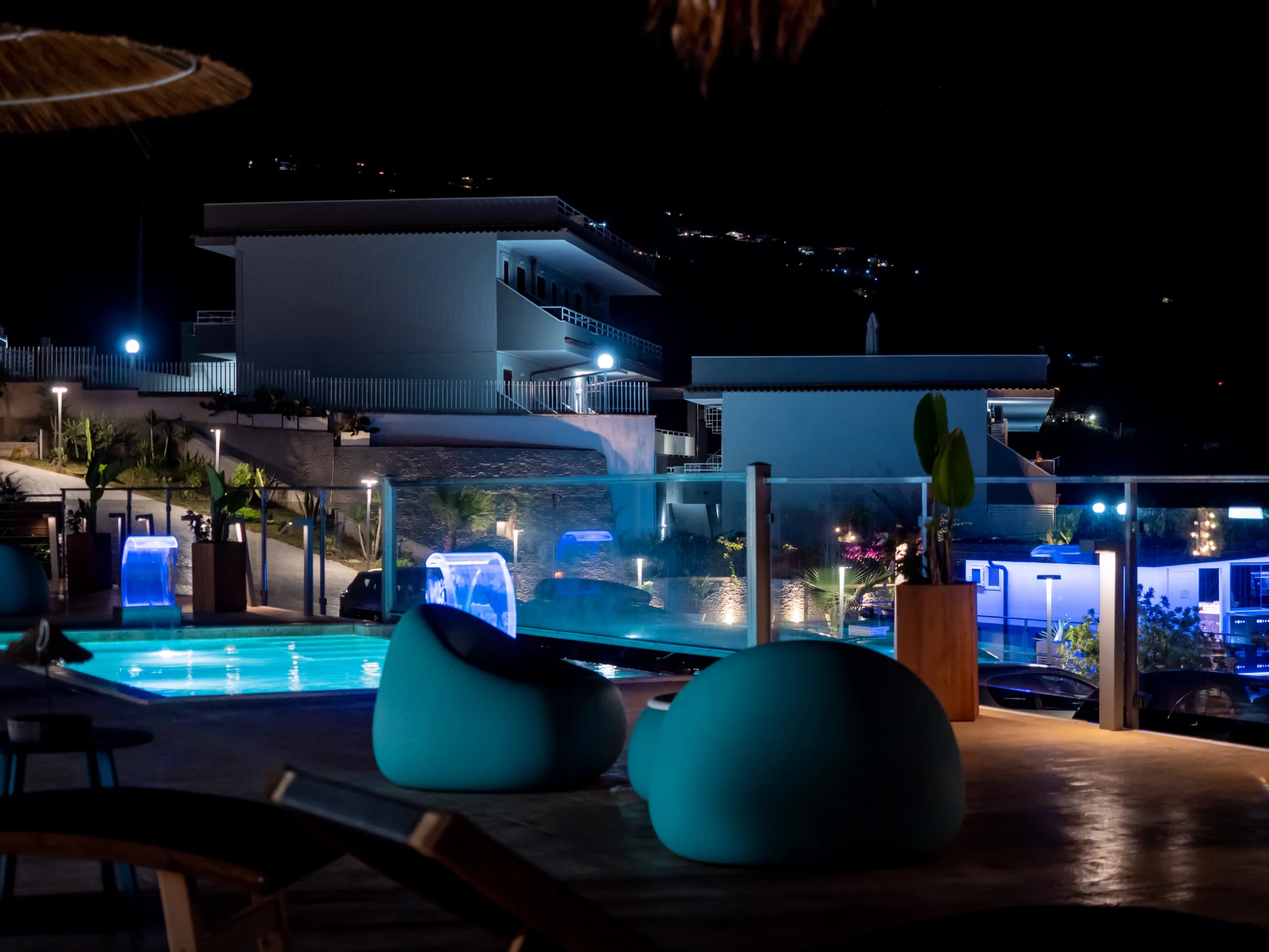 Vista notturna dell'area lounge bar con poltrone moderne e piscina illuminata presso l'Airone Residence Zambrone in Calabria.
