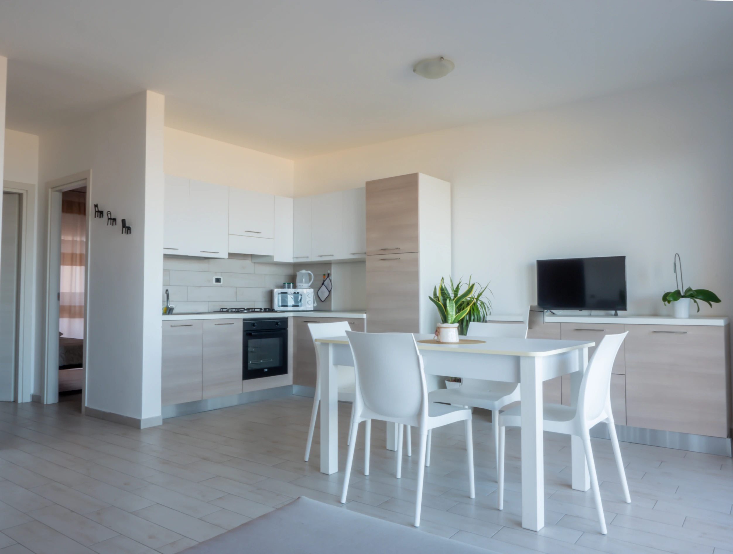 Zona giorno moderna con angolo cottura completo, tavolo da pranzo bianco e TV in un appartamento dell'Airone Residence Zambrone.