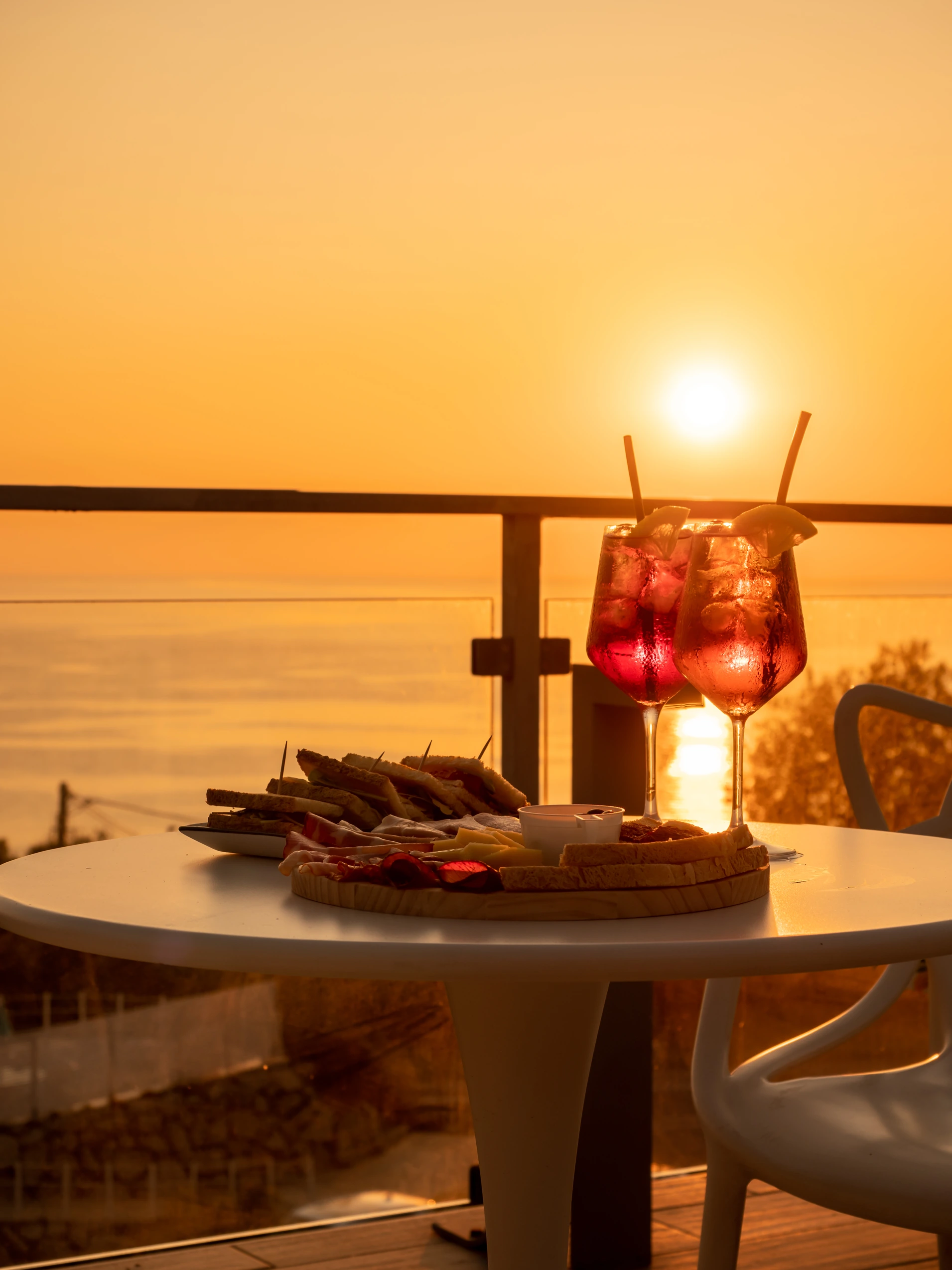 Aperitivo al tramonto vista mare sulla terrazza dell'Airone Residence Zambrone con due calici di spritz e un tagliere di salumi.