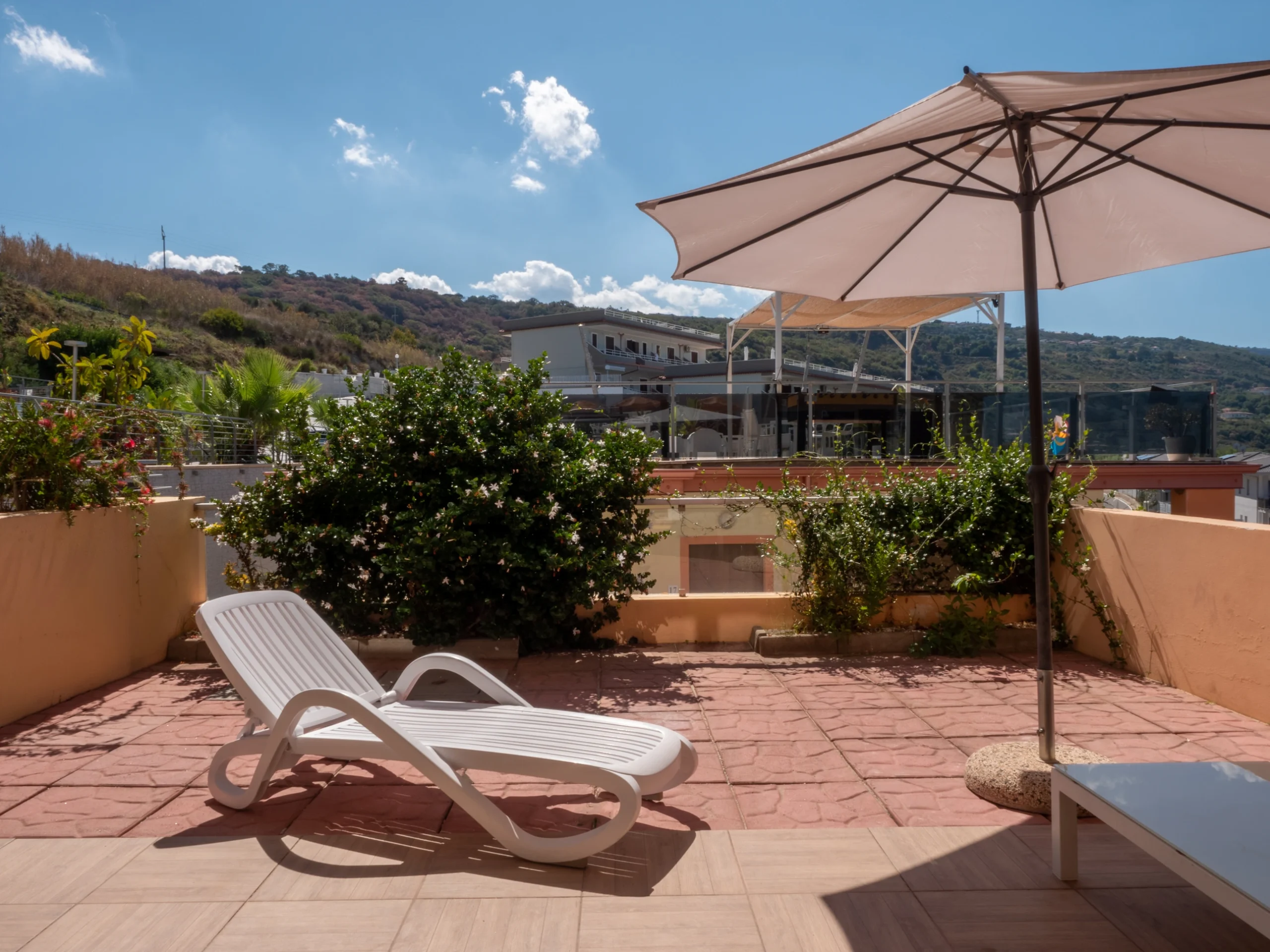 Lettino prendisole bianco e ombrellone aperto sul terrazzo solarium panoramico dell'Airone Residence Zambrone, Calabria.